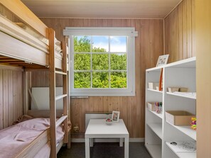 Ein Zimmer mit Etagenbetten, einem Fenster mit Blick ins Grüne, einem kleinen Tisch mit Bilderrahmen und Regalen mit verschiedenen Gegenständen.