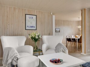 Un salon moderne avec des meubles blancs, une œuvre d’art encadrée au mur et un coin repas à l’arrière-plan.