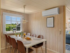Ein Essbereich mit einem für sechs Personen gedeckten Tisch, umgeben von Holzwandverkleidungen, einem Fenster mit Aussicht und einer an der Wand montierten Klimaanlage.