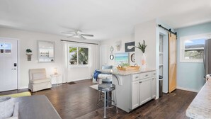 A spacious living area with a kitchen, a dining table, and a bar stool. - Walk to Surfside Beach Access, Golf Cart Add On (St. Augustine)