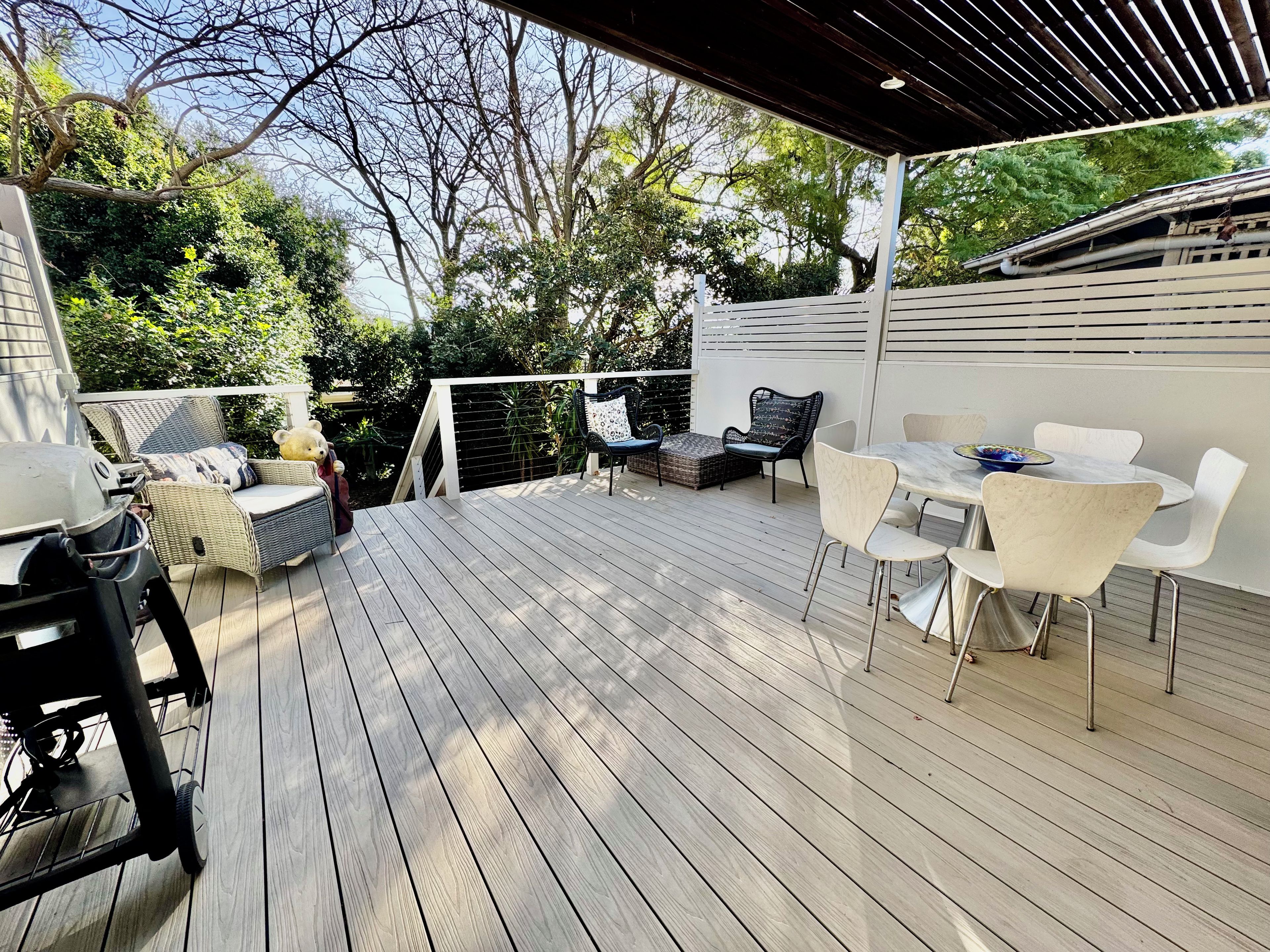 Eine überdachte Terrasse mit Gartenmöbeln, einem Grill und einem Esstisch.