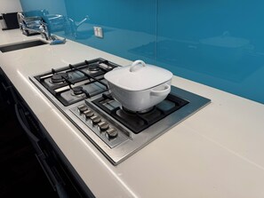 A modern kitchen with a gas stove, a pot on the burner, and a blue wall in the background.
