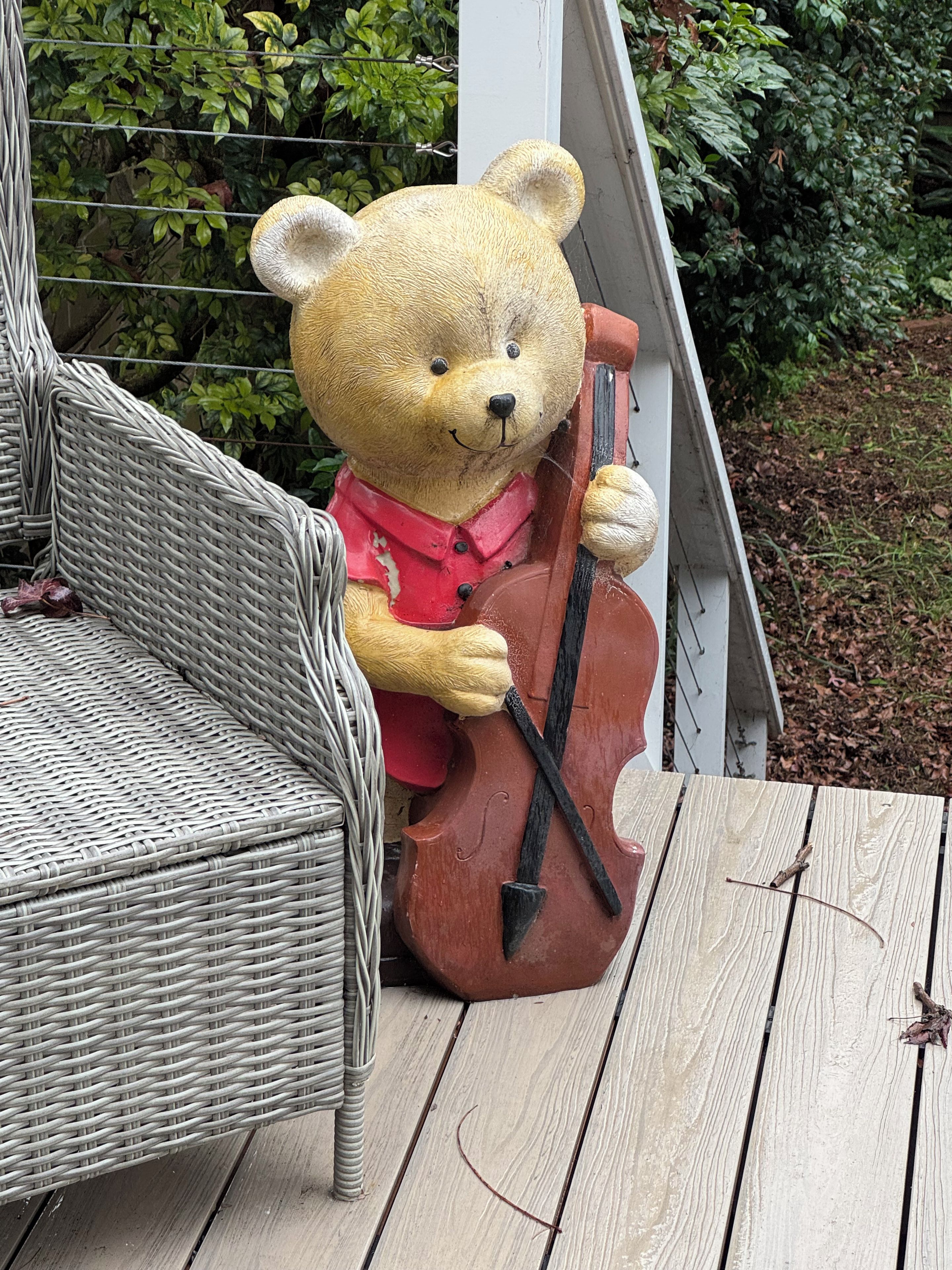 Une chaise en osier et une statue d’ours tenant un violoncelle, le tout sur une terrasse en bois.