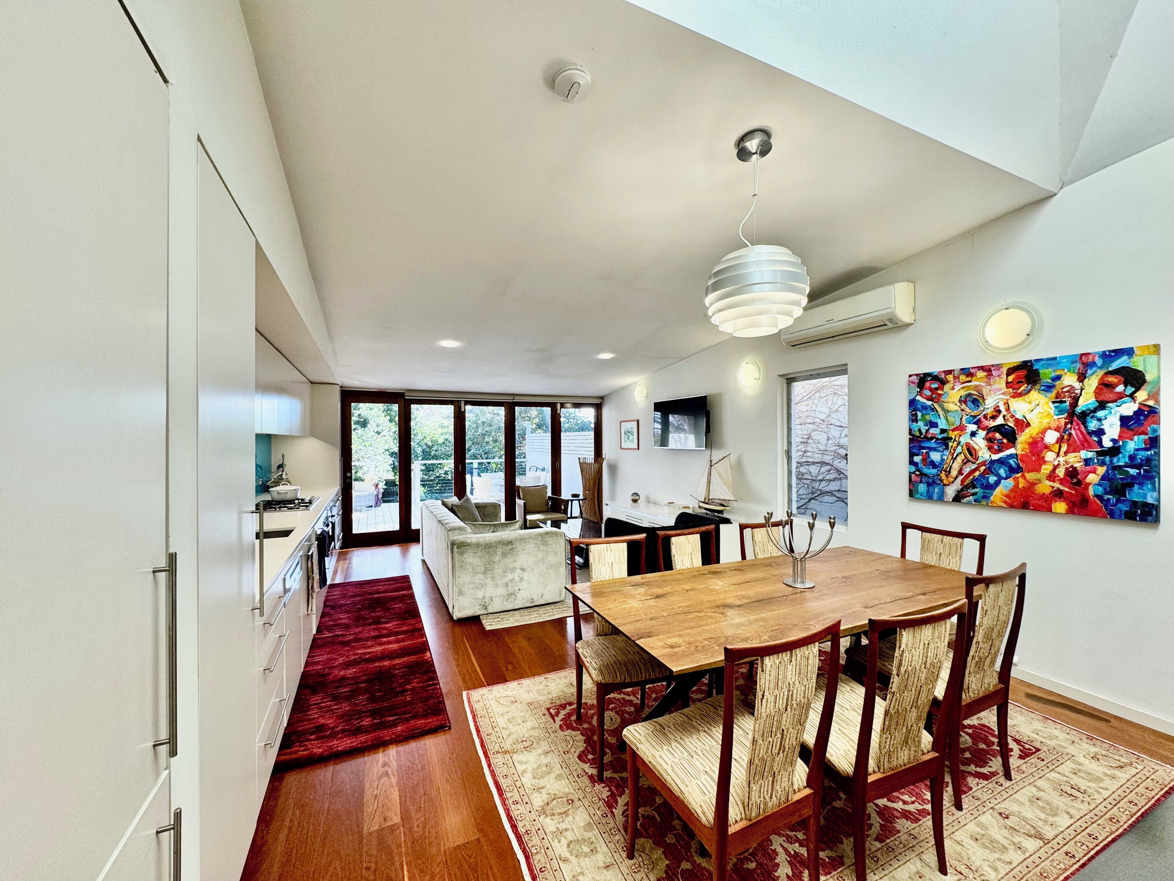 A modern dining area with a wooden table and chairs, a red rug, and a large abstract painting on the wall.