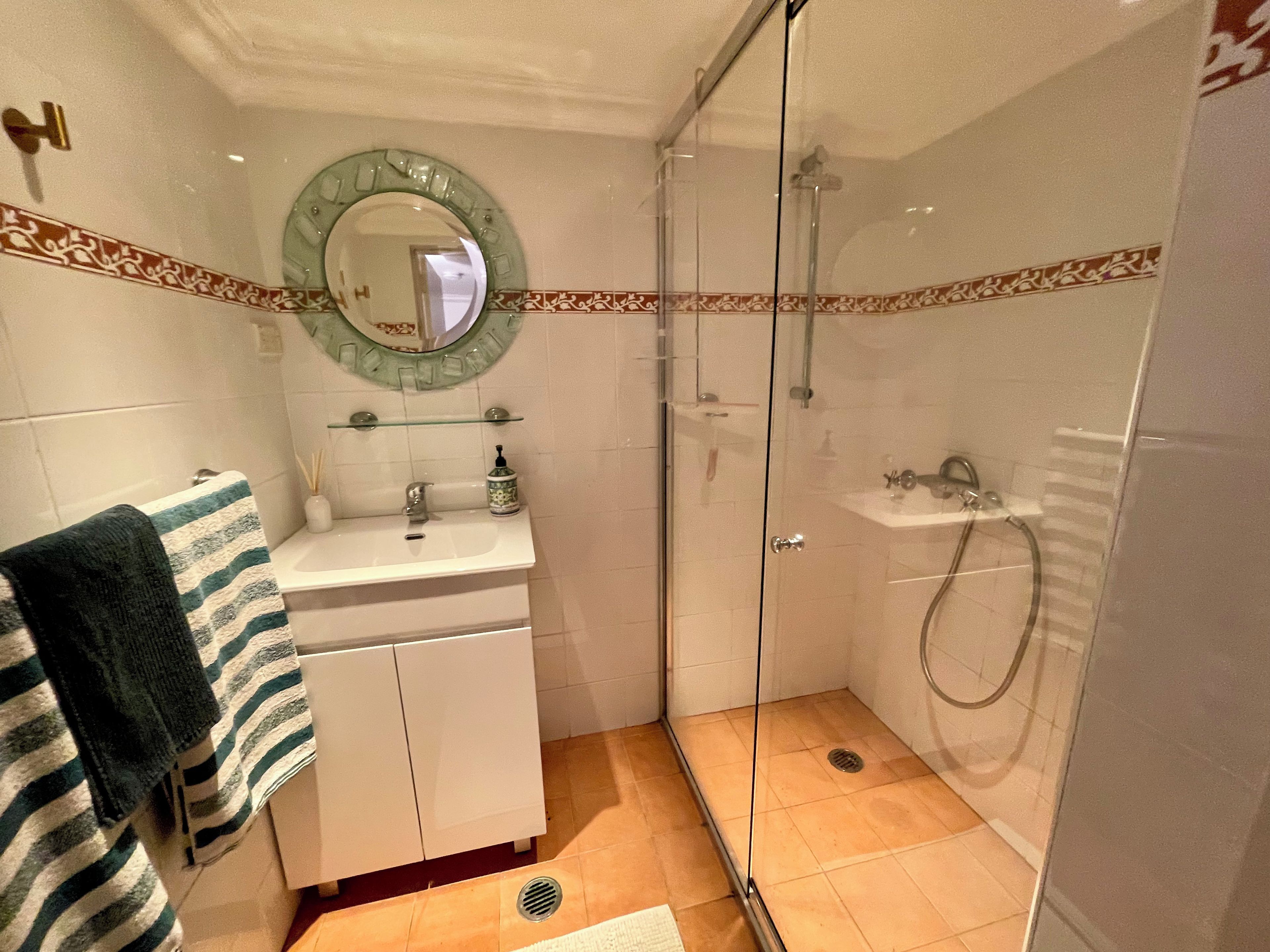 A bathroom with a glass-enclosed shower, a sink with a mirror above it, and a towel hanging on the wall.