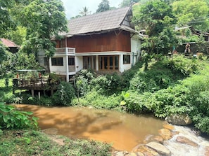 A wooden house with a balcony, surrounded by lush greenery and a small stream. - T-Valley Maekampong (Mae On)