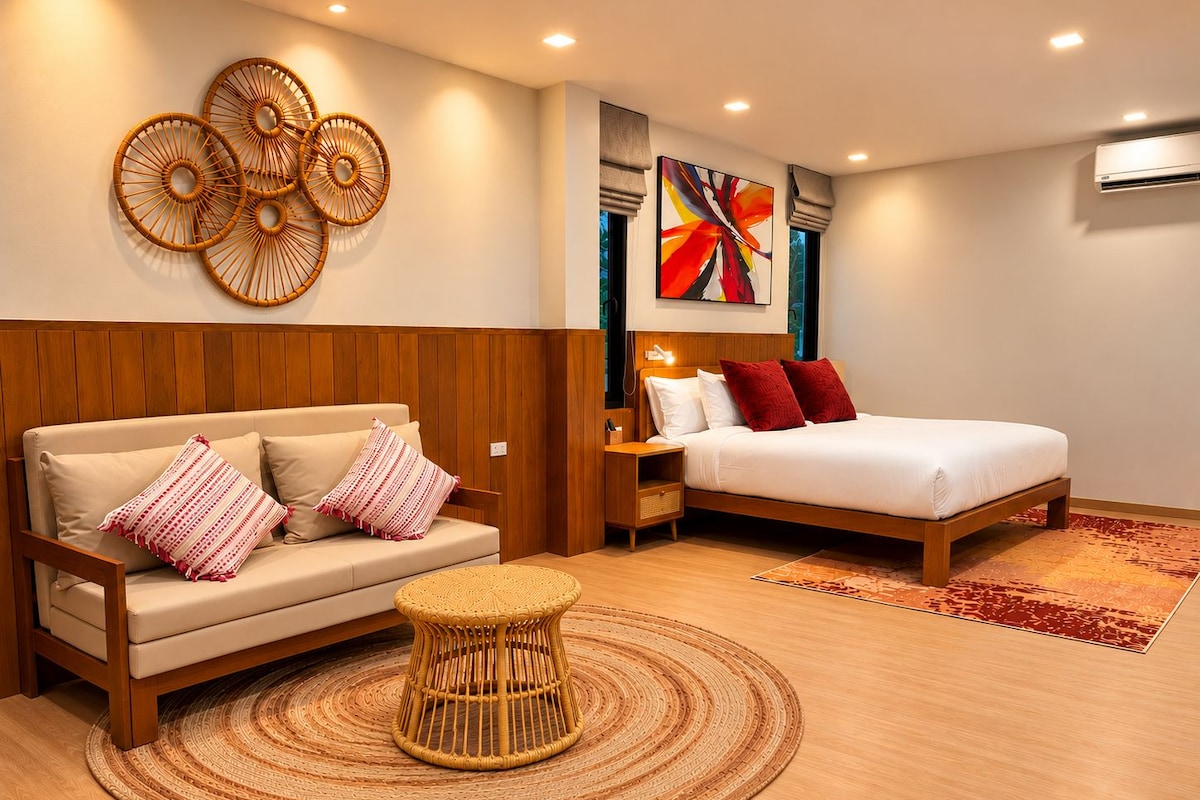 Quarto de hotel moderno com cama de cabeceira em madeira, sofá com almofadas estampadas, um banquinho trançado e uma grande pintura abstrata na parede.