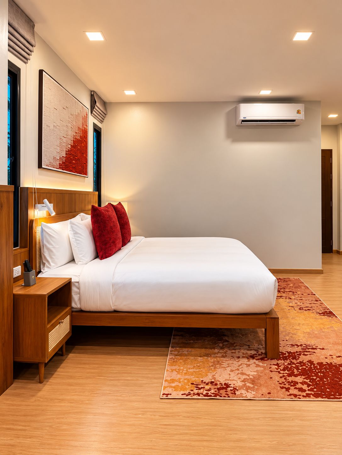 Ein modernes Hotelzimmer mit einem großen Bett, einem Holfnachtkästchen, einem Beistelltisch, einer wandmontierten Klimaanlage und einem gemusterten Teppich.