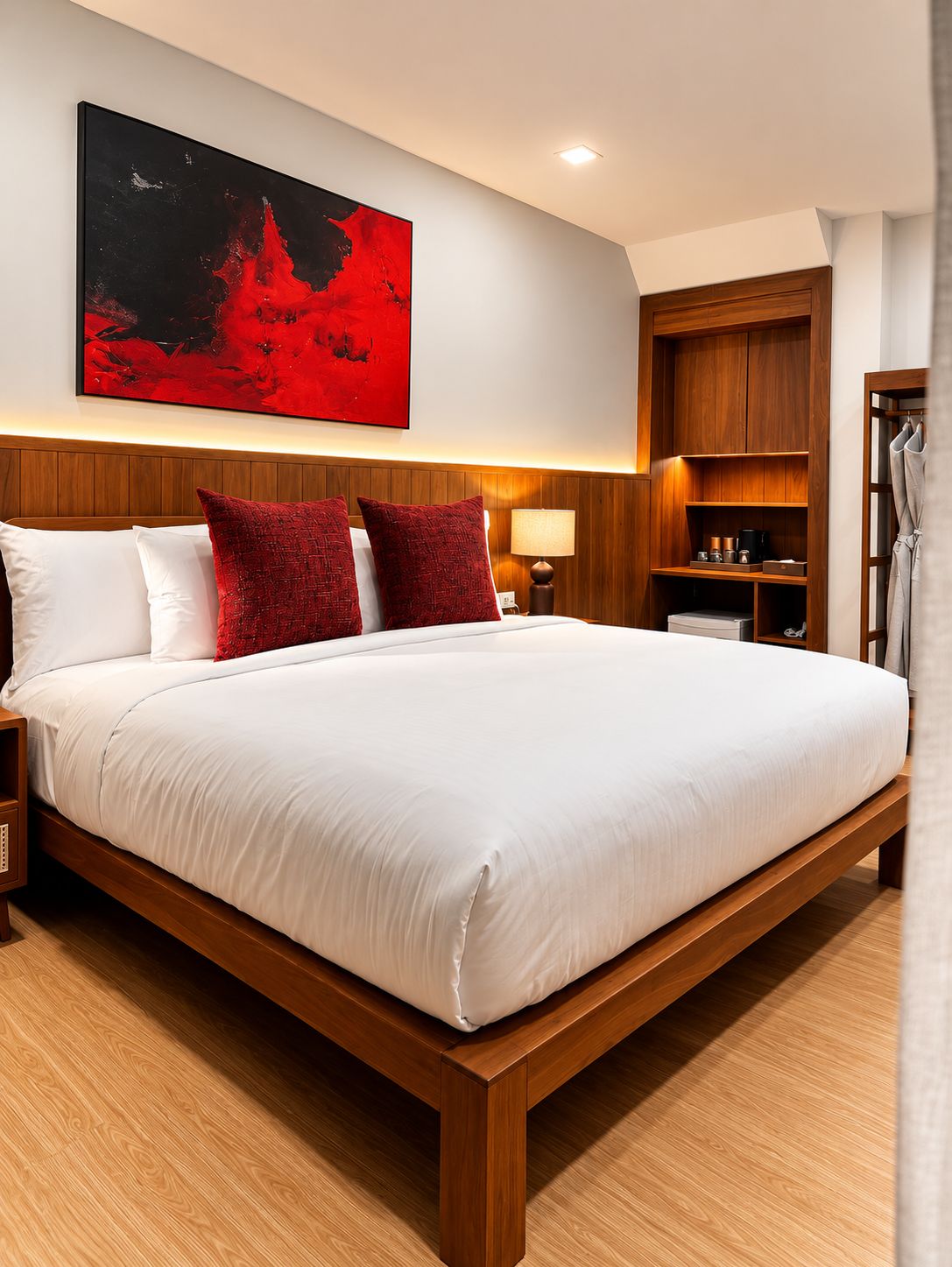 A hotel room with a large bed, wooden headboard, a red abstract painting, a nightstand, a bedside table with a lamp, and a wooden wardrobe.