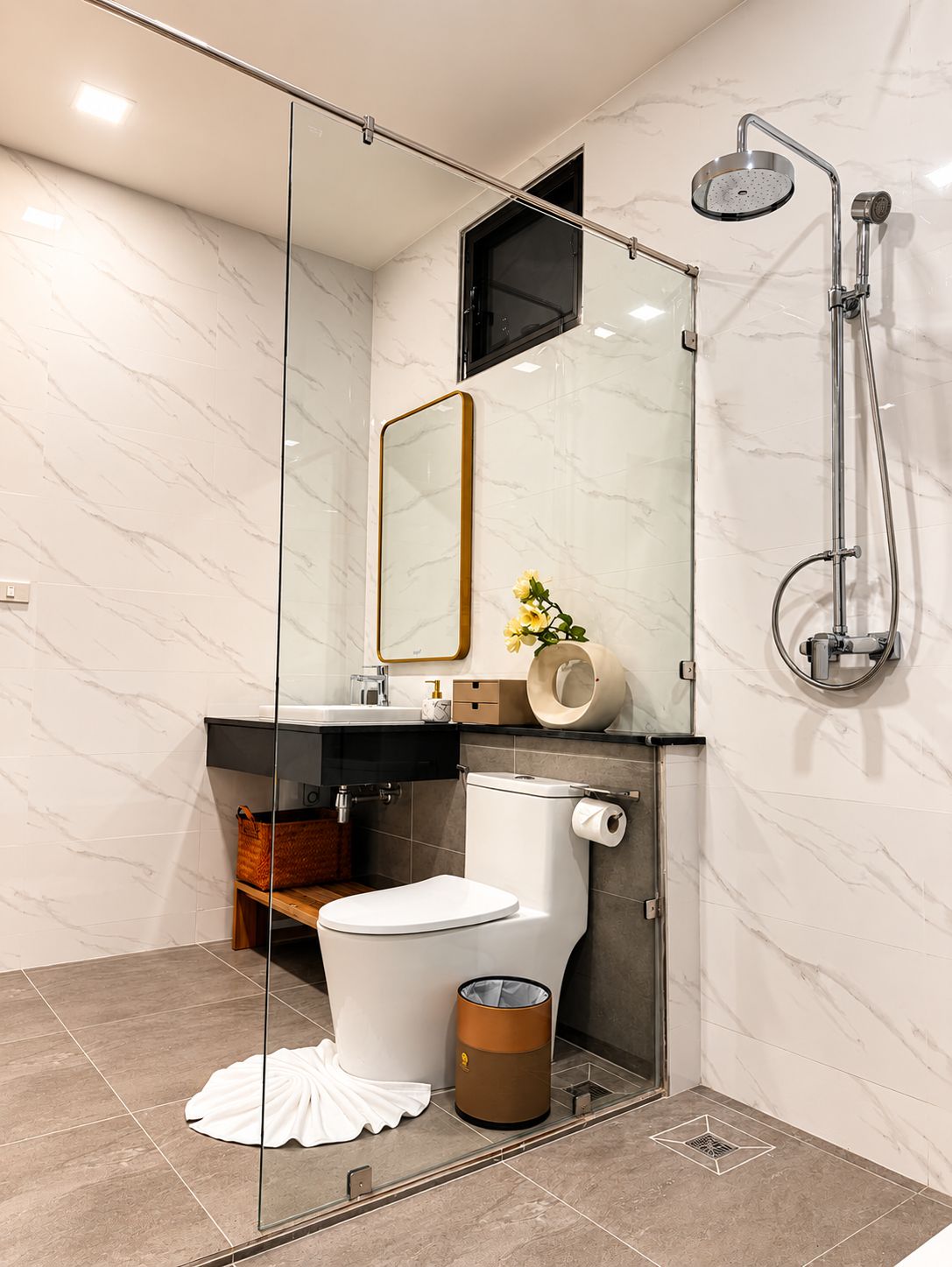 A modern bathroom with a glass shower enclosure, a toilet, a sink with a mirror, and a trash can.