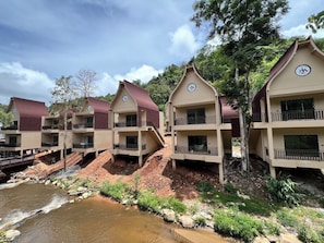 A row of multi-story buildings with balconies, situated by a river. - T-Valley Maekampong  (Mae On)