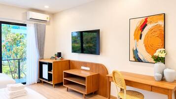 A modern hotel room with a wooden desk, a television, a large abstract painting, and a view of greenery outside.