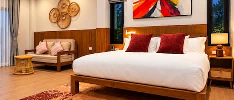 Un dormitorio moderno con una cama grande, cabecera de madera, mesita de noche con lámpara, una obra de arte en la pared y un área de descanso con una silla y cojines.