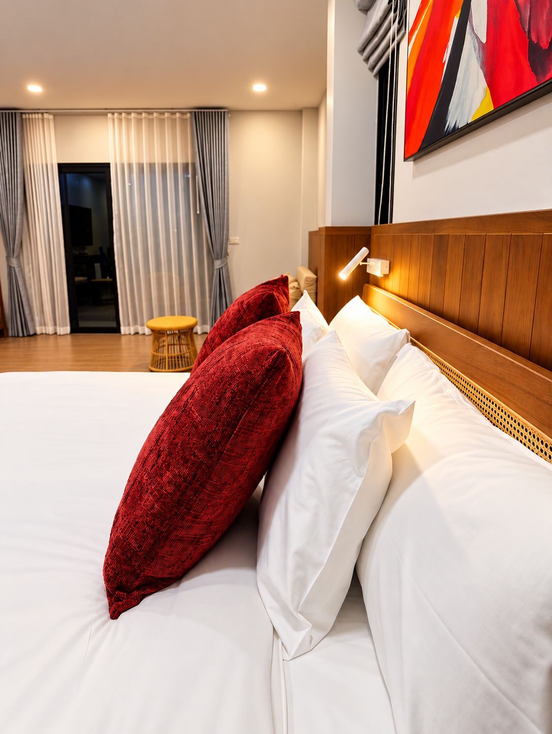 Habitación de hotel con una cama, una mesita de noche, una lámpara, un cuadro y vistas al exterior por la ventana.