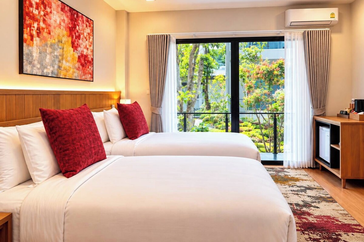 Quarto de hotel com uma cama grande, escrivaninha, ar condicionado e janela com vista para o verde.