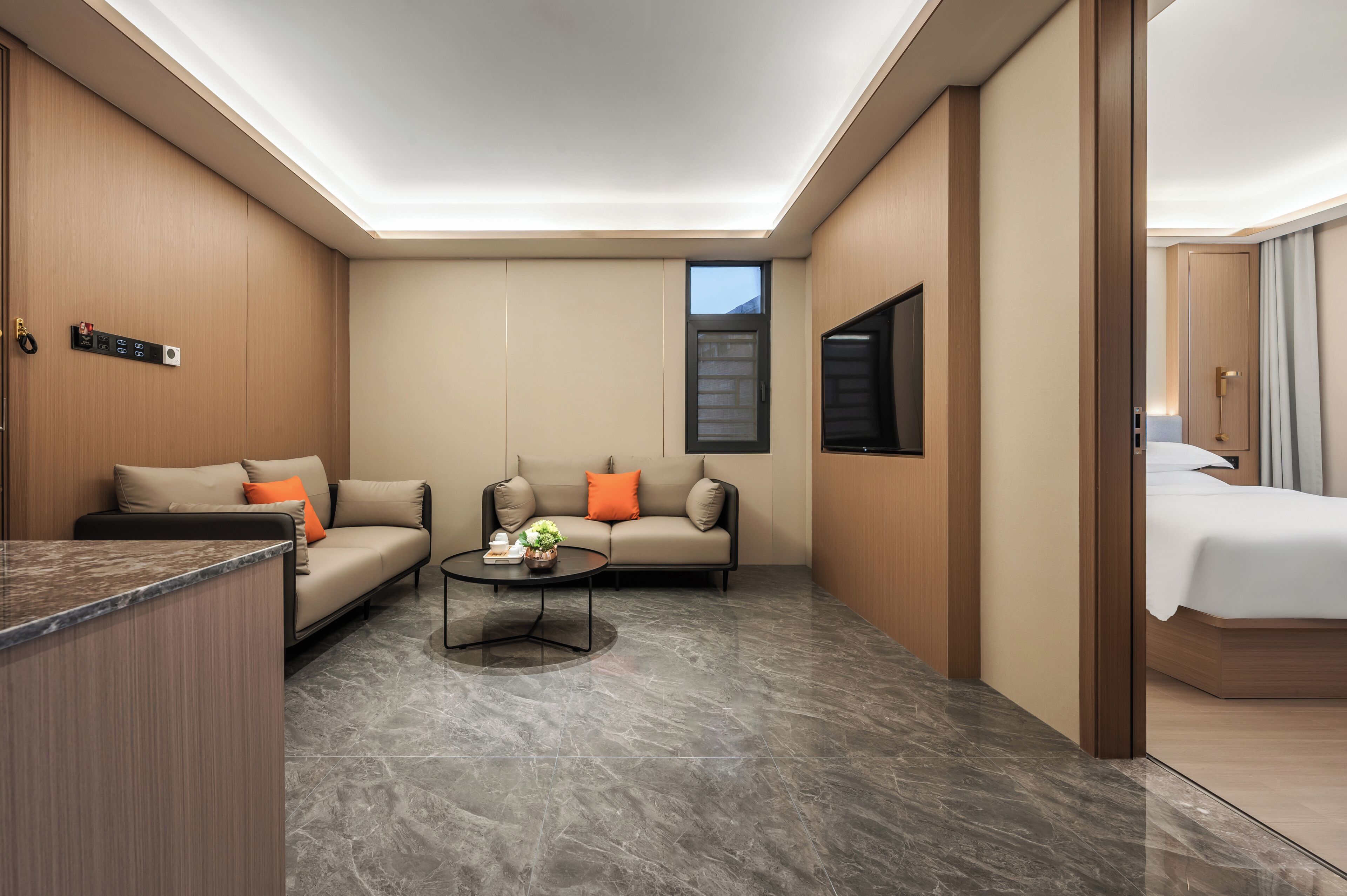 A modern hotel room with a sofa, a coffee table, a bed, and a TV.