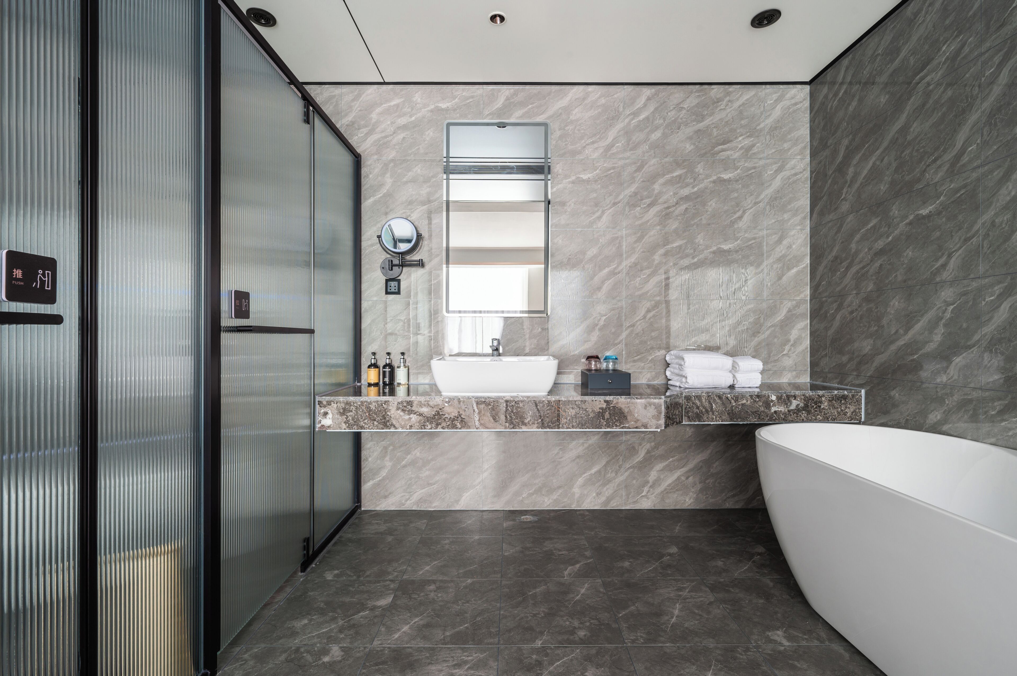 A modern bathroom with a glass shower enclosure, a large mirror, a white sink, and a freestanding bathtub.