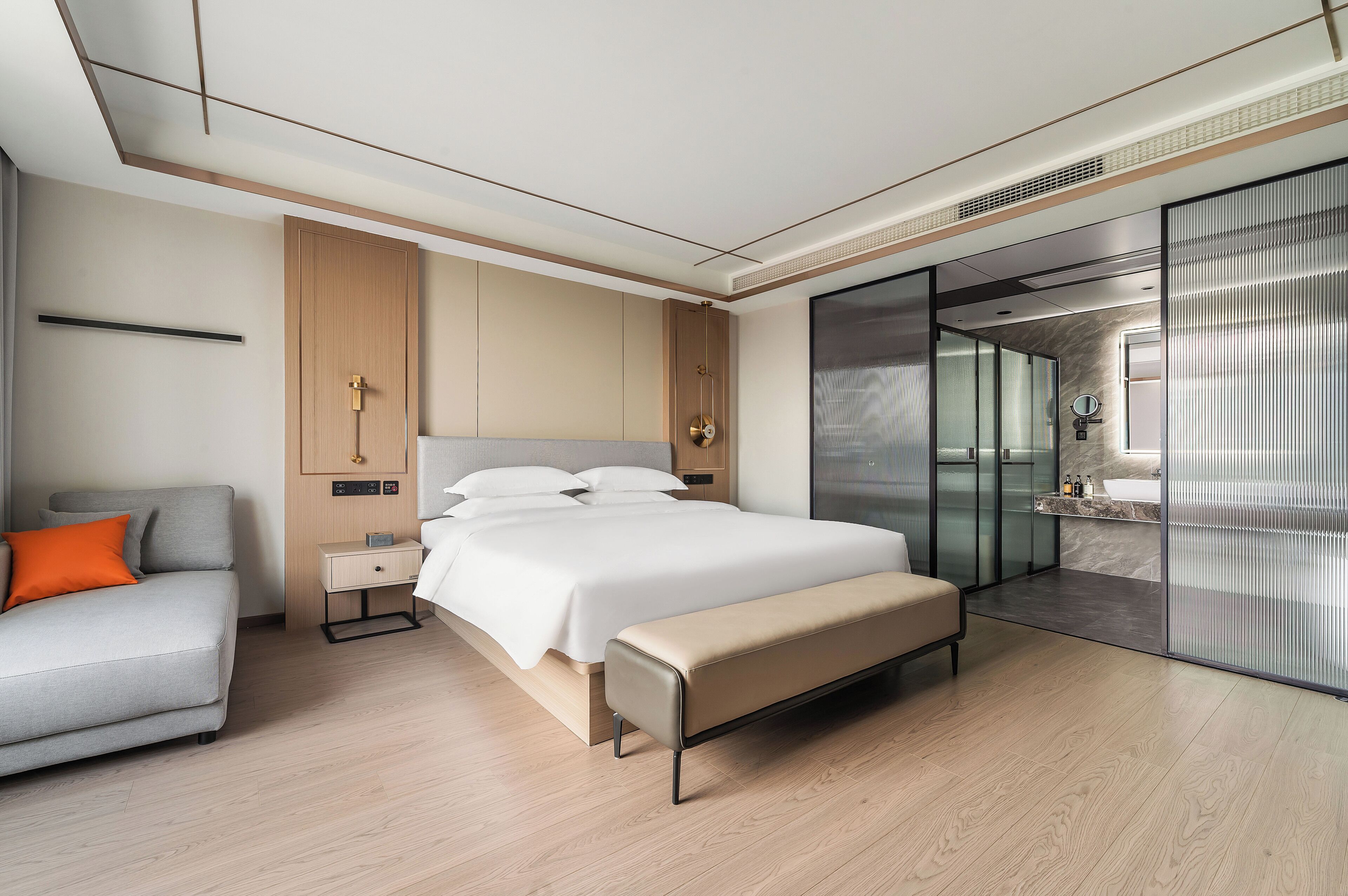 Ein modernes Hotelzimmer mit Bett, Nachttisch, Bank und einer Sitzecke mit Sofa.