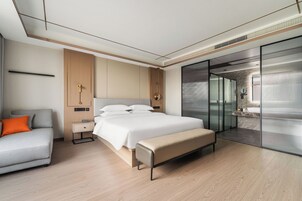 Una habitación de hotel moderna con cama, mesita de noche, banco y un área de descanso con sofá.