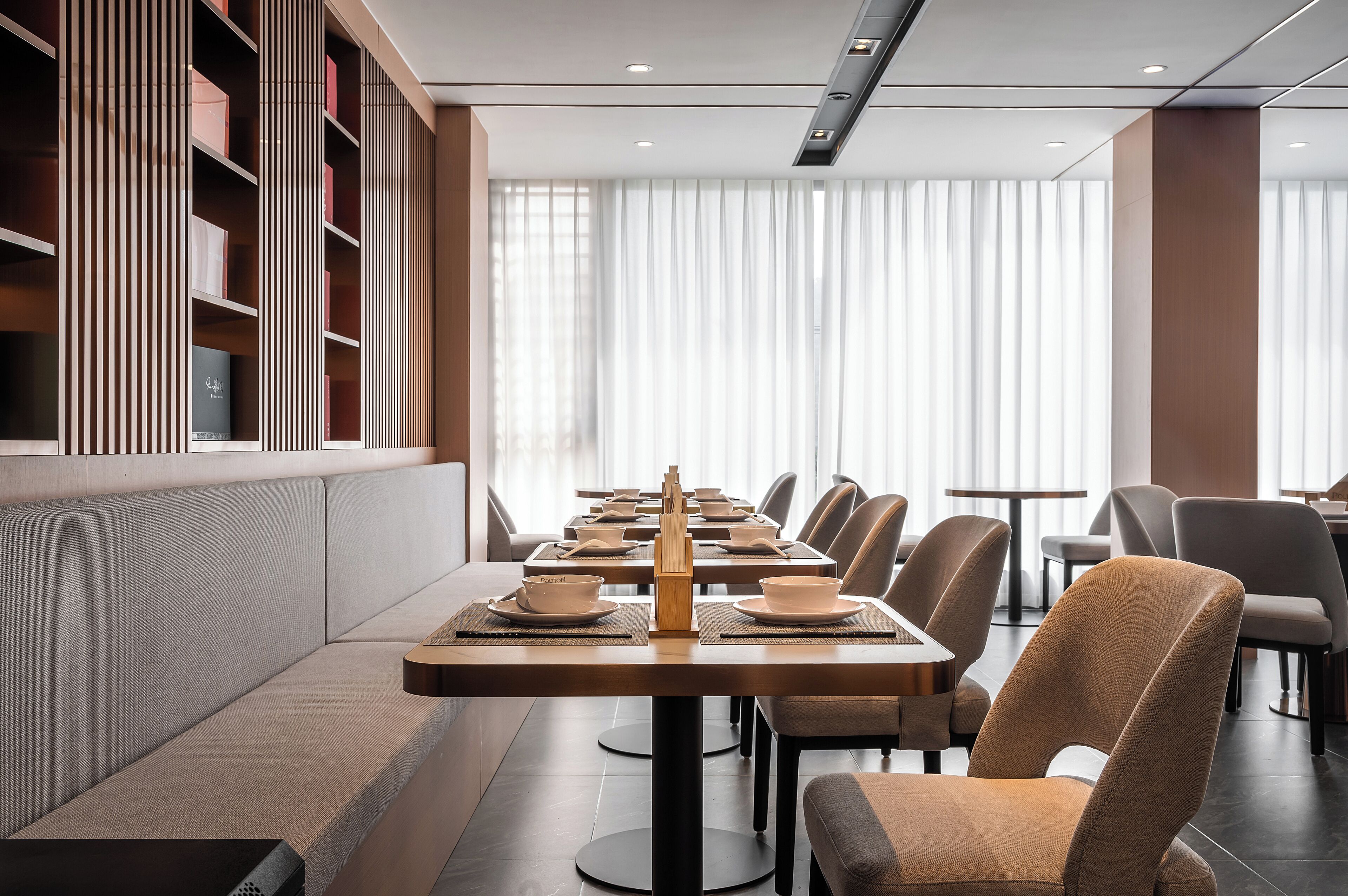 A modern dining area with long tables, chairs, and a bookshelf.