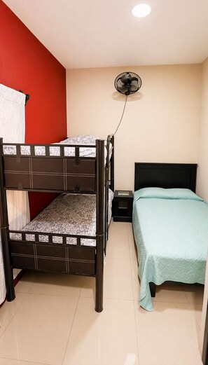 A room with a bunk bed, a single bed, a nightstand, and a wall-mounted fan. - Socrates House (Tequila)