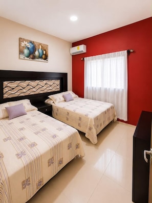 A hotel room with two beds, a red accent wall, a painting, and an air conditioning unit.