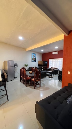A spacious living area with a dining table, chairs, a sofa, and a TV.