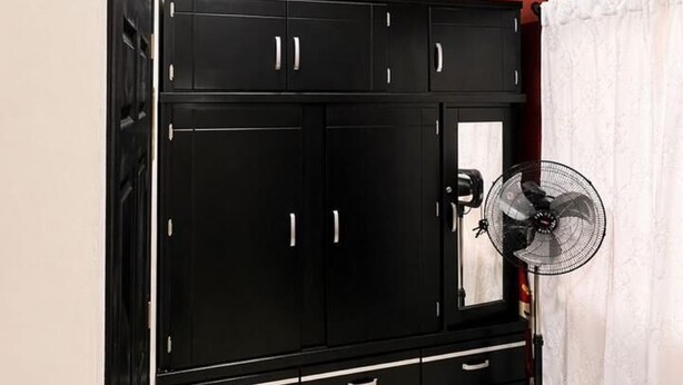 A room with a black wardrobe, a standing fan, and a white curtain. - Socrates House (Tequila)