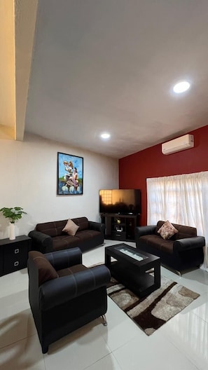 A living room with a sofa set, a coffee table, a flat-screen TV, and a painting on the wall.