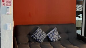 A room with a red wall, a framed painting, a dark sofa with patterned cushions, and a visible door. - Socrates House (Tequila)