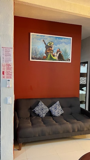 Ein Zimmer mit roter Wand, einem gerahmten Gemälde, einem dunklen Sofa mit gemusterten Kissen und einer sichtbaren Tür.