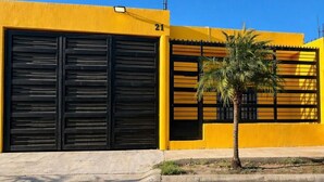 A building with a yellow facade, black shutters, and a palm tree in front. - Socrates House (Tequila)
