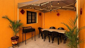 A covered outdoor seating area with a table and chairs, potted plants, and a window with a grid pattern. - Socrates House (Tequila)