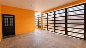 A room with a wooden floor, a black door, and large windows with horizontal blinds. - Socrates House (Tequila)