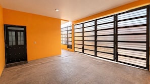 Ein Zimmer mit Holzboden, einer schwarzen Tür und großen Fenstern mit horizontalen Rollläden.
