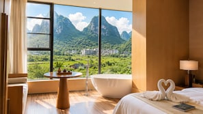 A modern hotel room with a large window, a bathtub, a round table with a vase and teapot, and a bed with towels shaped like swans. - The Floral Dreamscape Retreat -Yulong Romance Park Branch-Tickets Reservation & Day Tour Arrangement (Guilin)