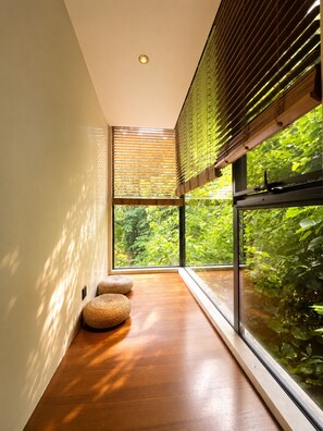 Un interior moderno con ventanas amplias, piso de madera y pufs tejidos.