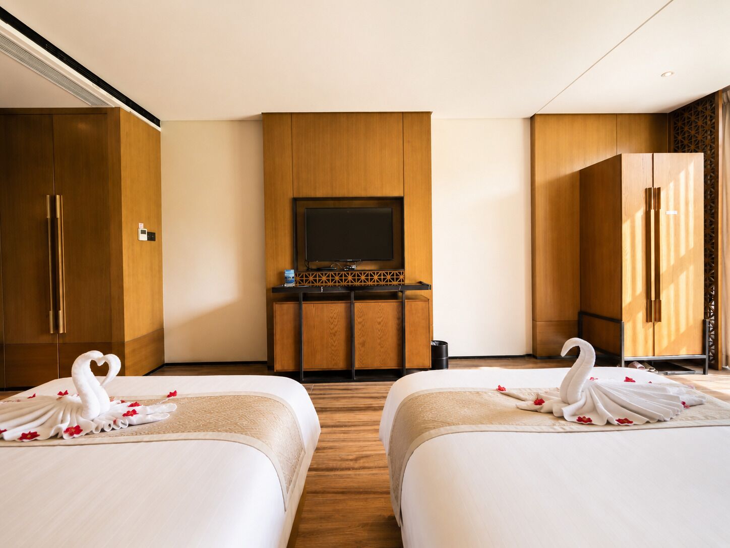 A hotel room with two beds, a television, wooden cabinets, and a minibar.