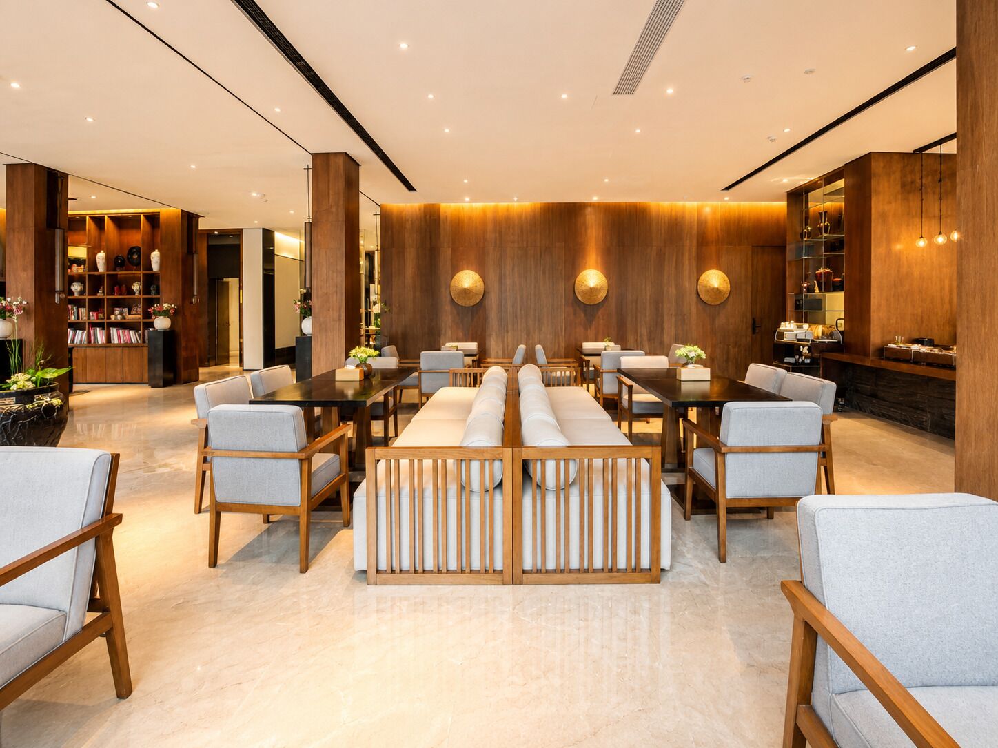 A modern hotel lobby with a central seating area, wooden paneling, and a bookshelf.
