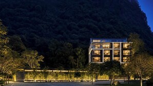 Un edificio moderno de varios pisos, rodeado de árboles y con una montaña al fondo.