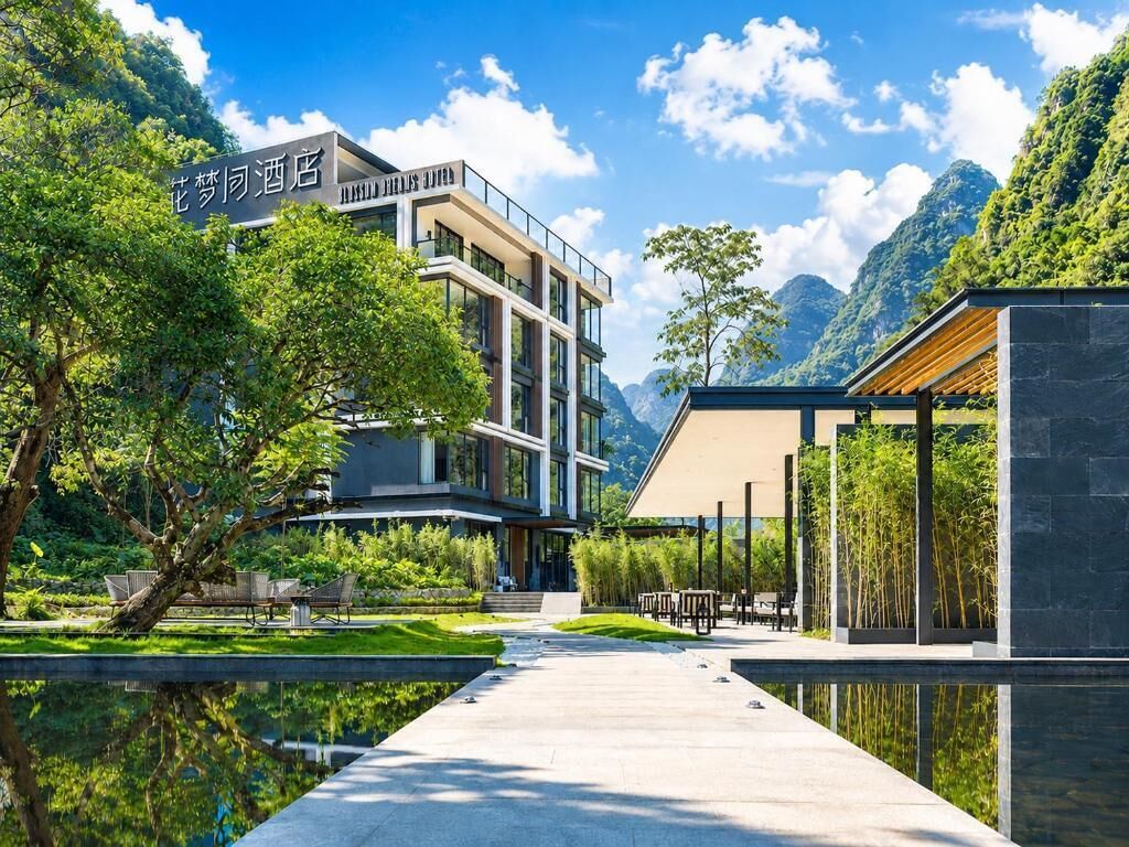 A modern hotel with a reflective pool, outdoor seating, and a mountainous backdrop.