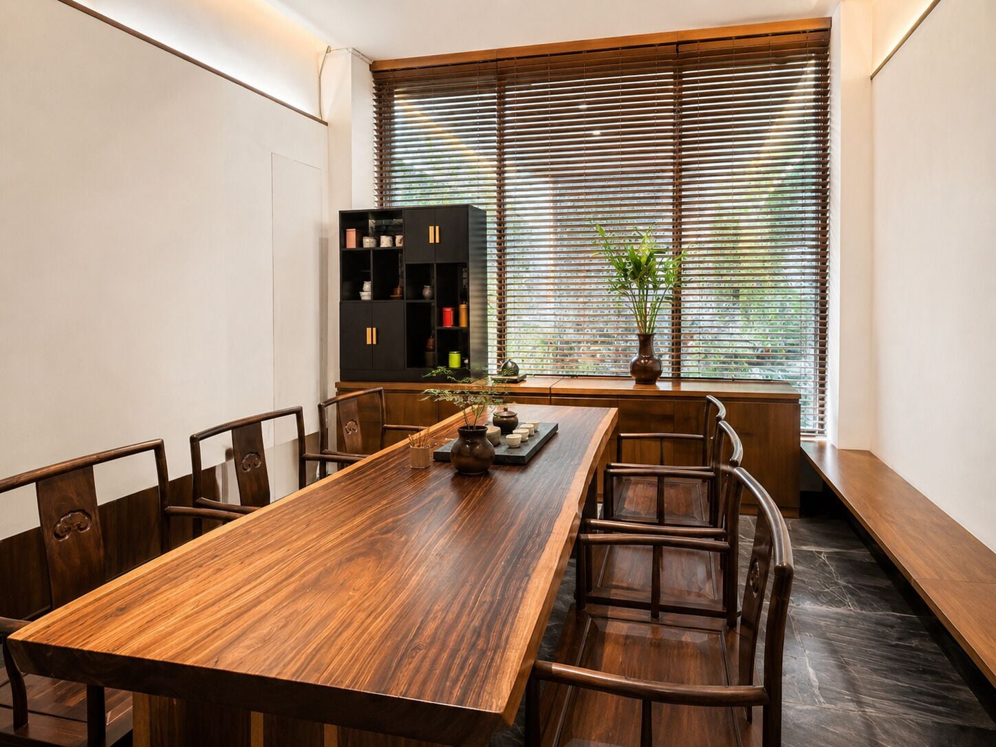 A dining area with a wooden table, chairs, a black cabinet, and a window with blinds.