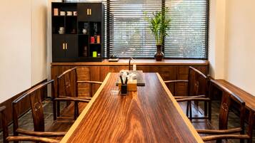 Un comedor con una mesa de madera larga, sillas, una estantería negra y una ventana con persianas.