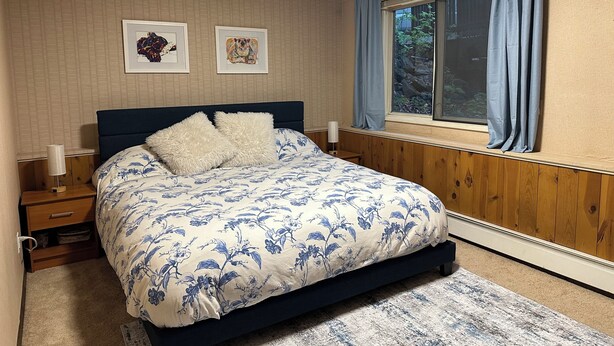 A bedroom with a bed, wooden paneling, a window with curtains, and two framed pictures on the wall. - 4BR/4BA Lakefront Lodge- mountain views, wildlife, canoeing- 9 min to airport (Anchorage)