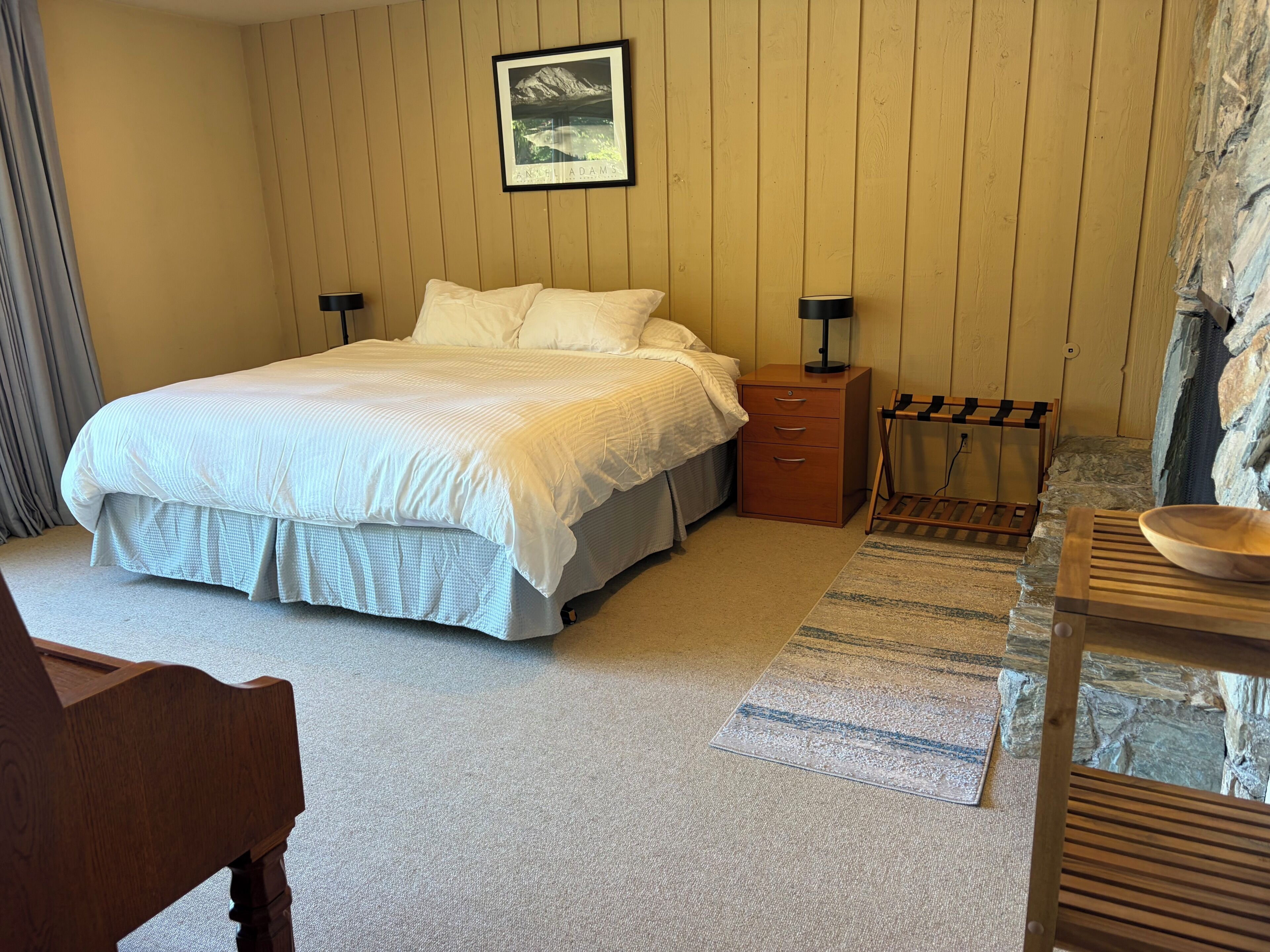 A bedroom with a bed, bedside tables, a desk, and a stone wall.
