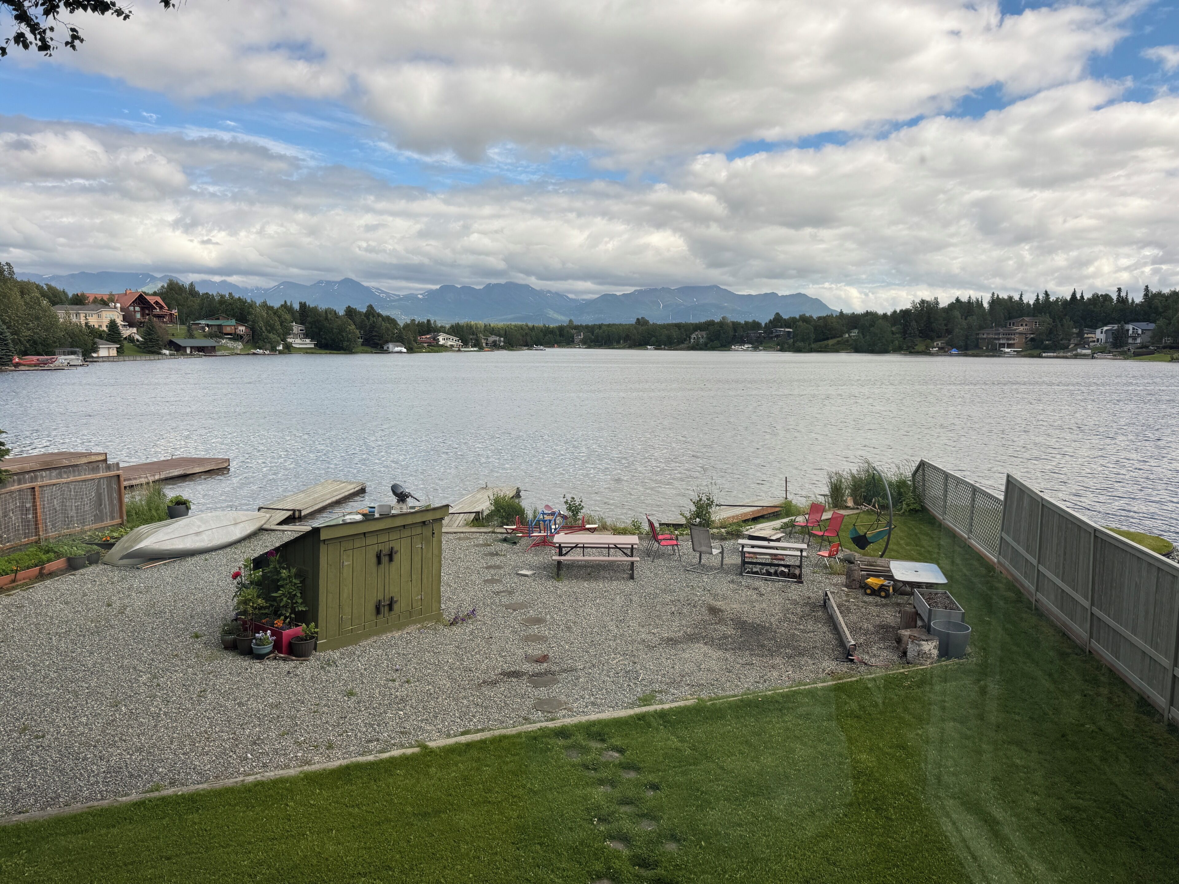 A lakeside property with a grassy area, a wooden dock, and a small shed.