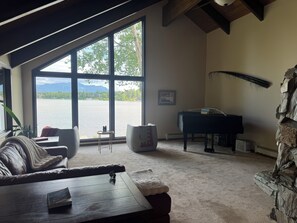 Ein Wohnzimmer mit Klavier, einer Couch, einem Couchtisch und einem großen Fenster mit Seeblick.