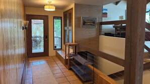 A hallway with a wooden floor, a staircase, a wall-mounted light fixture, and a door with a glass panel. - 4BR/4BA Lakefront Lodge- mountain views, wildlife, canoeing- 9 min to airport (Anchorage)