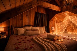 Un cuarto de madera acogedor y tenuemente iluminado, con una cama, una mesita con una lámpara y un dosel decorativo sobre una bañera.
