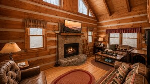 A log cabin interior with a fireplace, wooden walls, a sofa, and a view of the outdoors. - Romantic Private Forrest Hideaway + Heart Shaped Tub + Hot Tub! (Sevierville)